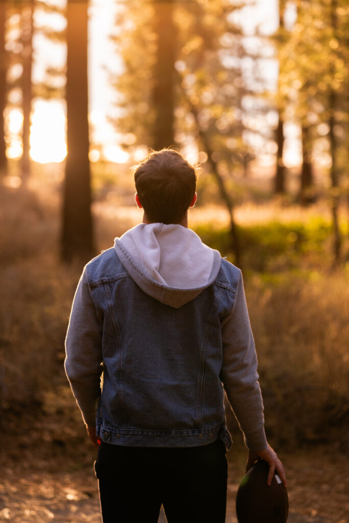 Senior standing with football at Lake Tahoe. Silhouette forest and lake