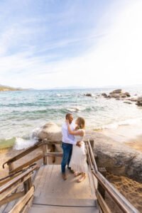 Romantic waves splash against the stairs at a hidden beach in Lake Tahoe with a couple about to kiss